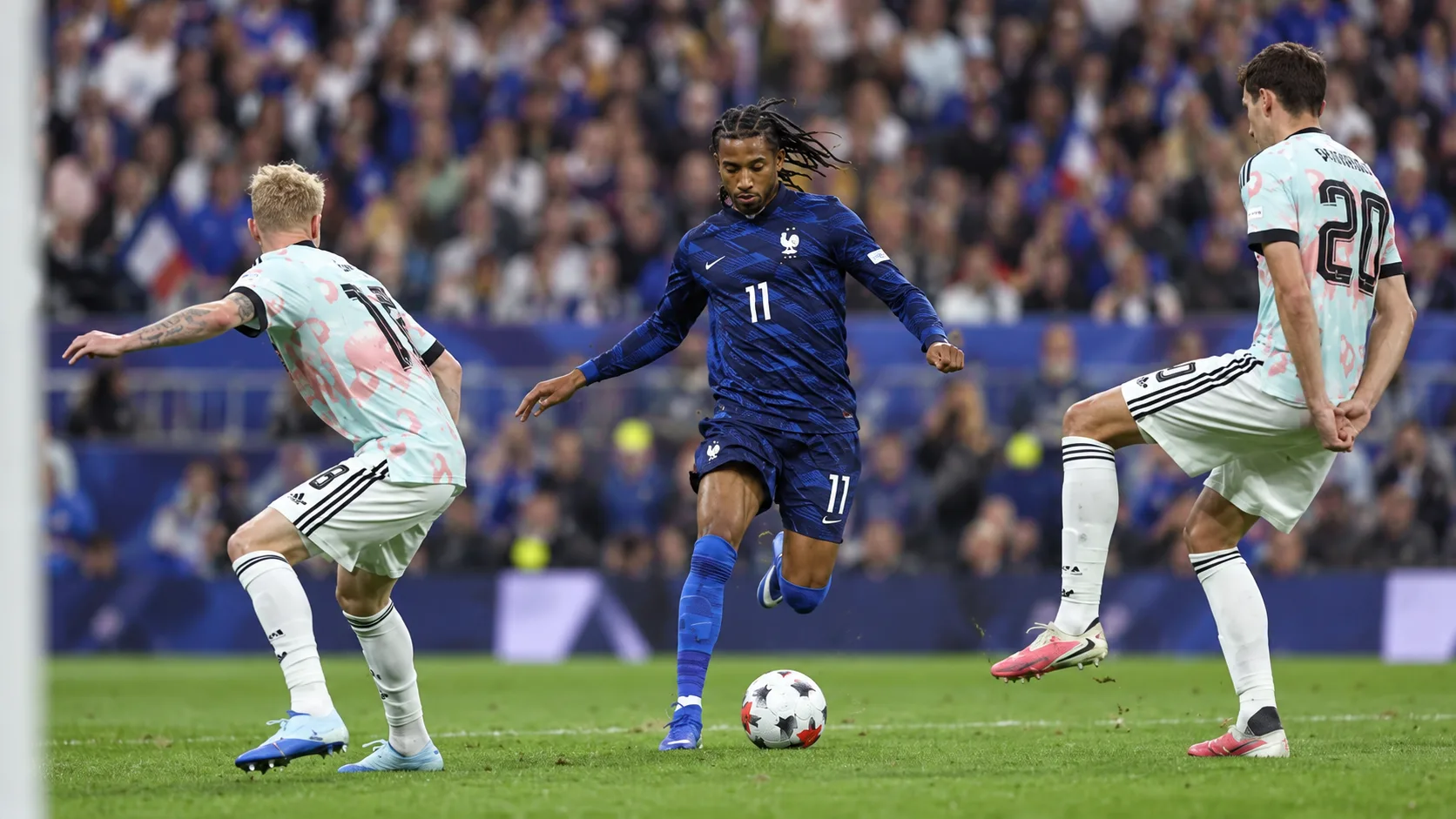 Ballon entre des joueurs en tenues bleues et rouges sur une pelouse, scène d’illustration d’un match international.