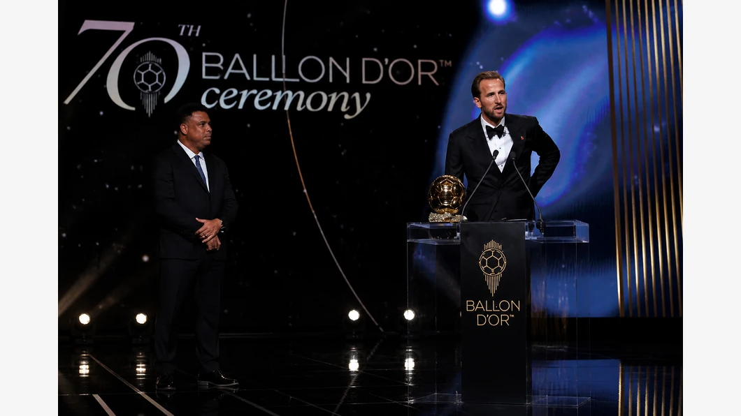 Harry Kane conduit le ballon et observe une option de passe sur la pelouse, illustrant son rôle dans la construction du jeu.