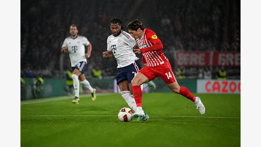 Michael Olise du Bayern et Lucas Höler de Freiburg se disputent le ballon au premier plan devant des tribunes floutées.